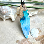 Surfbrett-Anhänger handgefertigt aus Maserholz & Harz in Blau-Weiß. Größe ca. 6,3 × 2 cm. Lederband verstellbar 26–47 cm, Schiebeknoten mit Holzperlen.