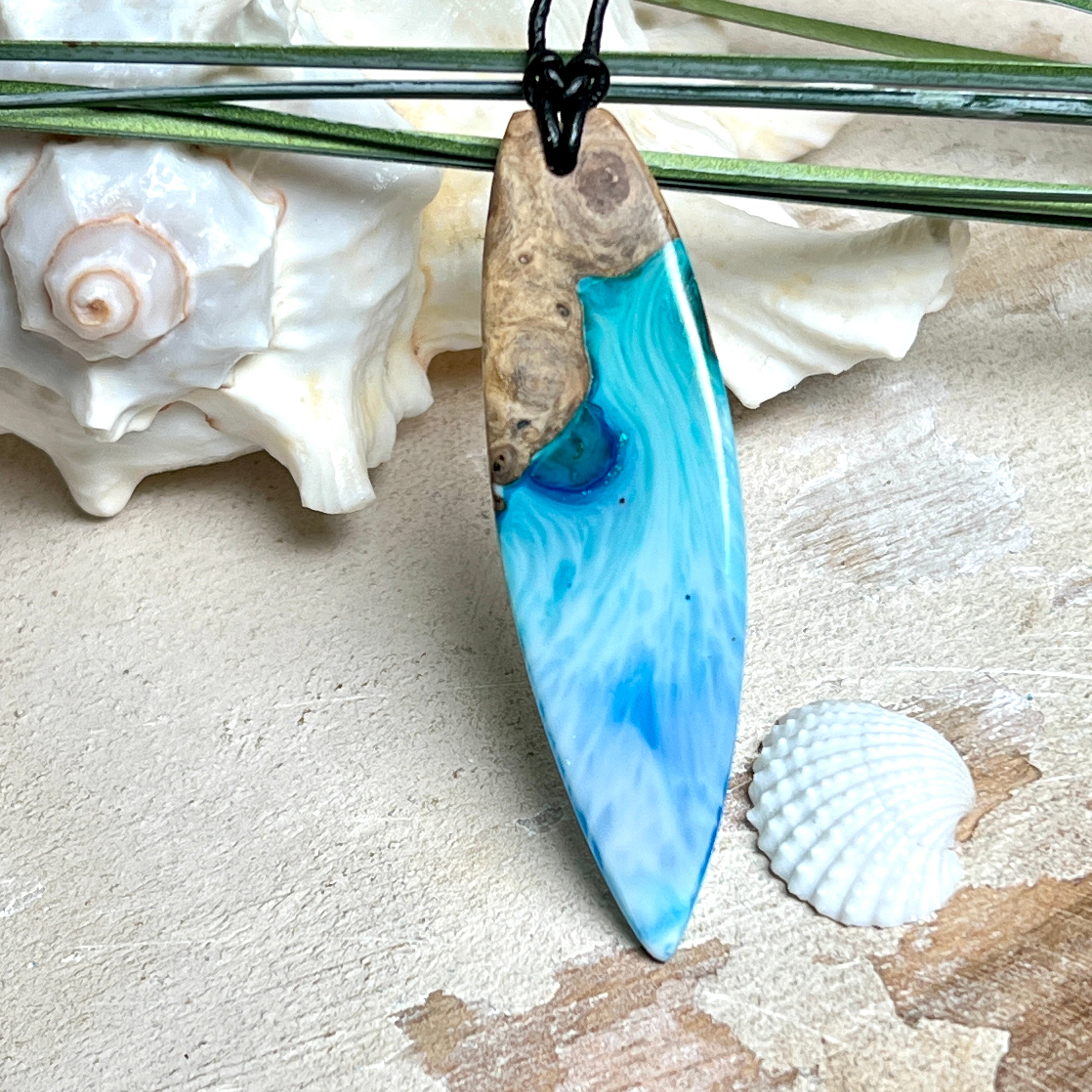 Surfbrett-Anhänger handgefertigt aus Maserholz & Harz in Blau-Weiß. Größe ca. 6,3 × 2 cm. Lederband verstellbar 26–47 cm, Schiebeknoten mit Holzperlen.