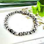 “Stilvolles Zebra-Achat-Armband mit schwarz-weißen Streifen auf hellem Untergrund, verziert mit goldenen Akzenten und grünen Blättern – ideal für Energiearbeit, spirituelle Balance und als modisches Accessoire.”