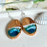 Handgefertigte Ohrringe „Wave Harmony“ aus Olivenholz und Epoxidharz in Blau-, Türkis- und Weißtönen. Das Design erinnert an Meereswellen am Strand. Jeder Ohrring ist ein Unikat mit individueller Maserung. Versilberte, nickelfreie und bleifreie Anhängerschlaufe, 925 Silber Ohrhaken. Maritimer Schmuck – perfekt für Meerliebhaber und als edles Geschenk.