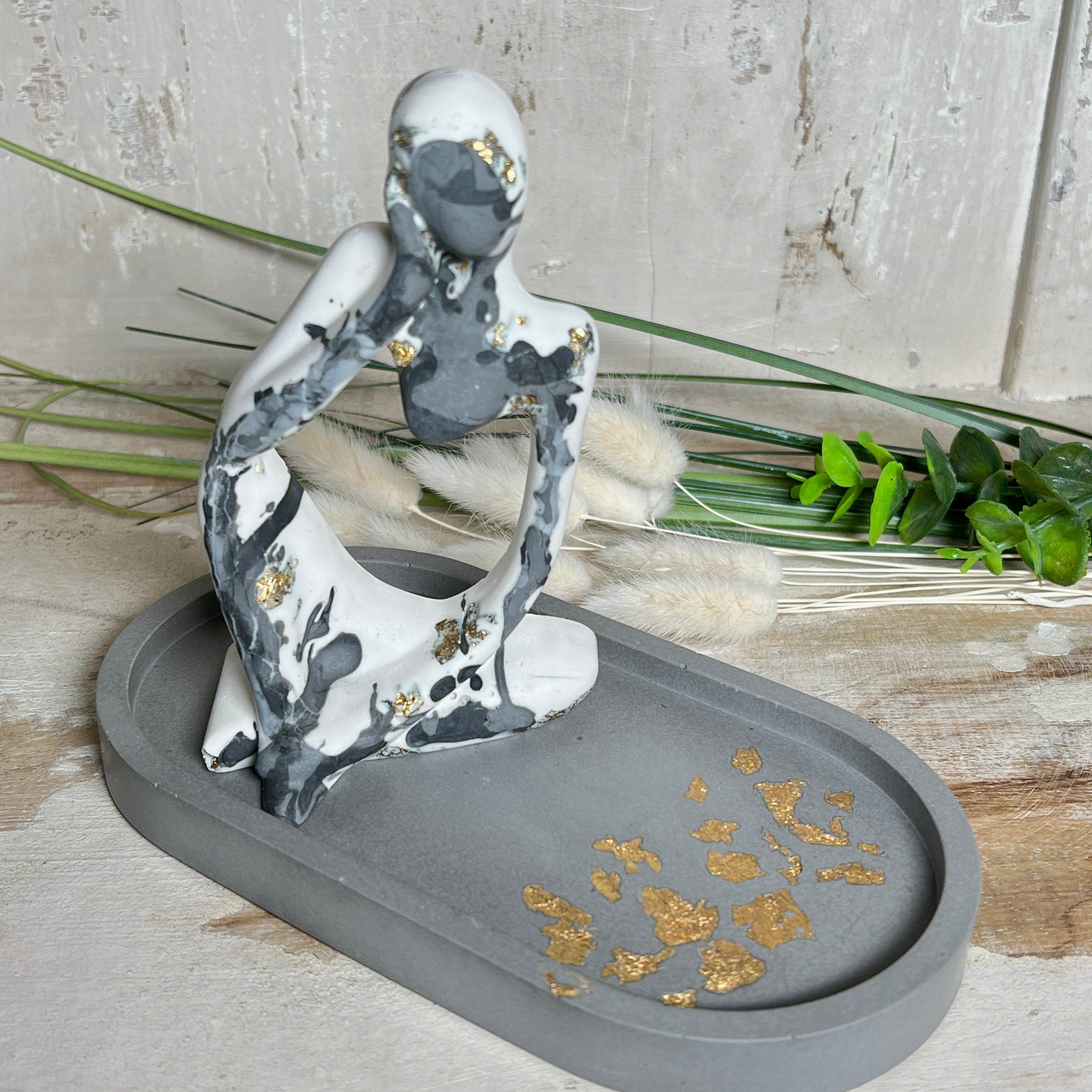 Handgefertigtes ovales Schmucktablett aus grauen  Jesmonite mit schimmernden Blattgold-Details. Die Unterseite ist mit vier Korkpunkten versehen und schützt empfindliche Oberflächen. Ideal zur stilvollen Aufbewahrung von Schmuck, Schlüsseln, Brille oder kleinen Dekoartikeln. Jedes Tablett ist ein Unikat mit individueller Maserung und goldenen Akzenten – Lieferung ohne Deko. Die 