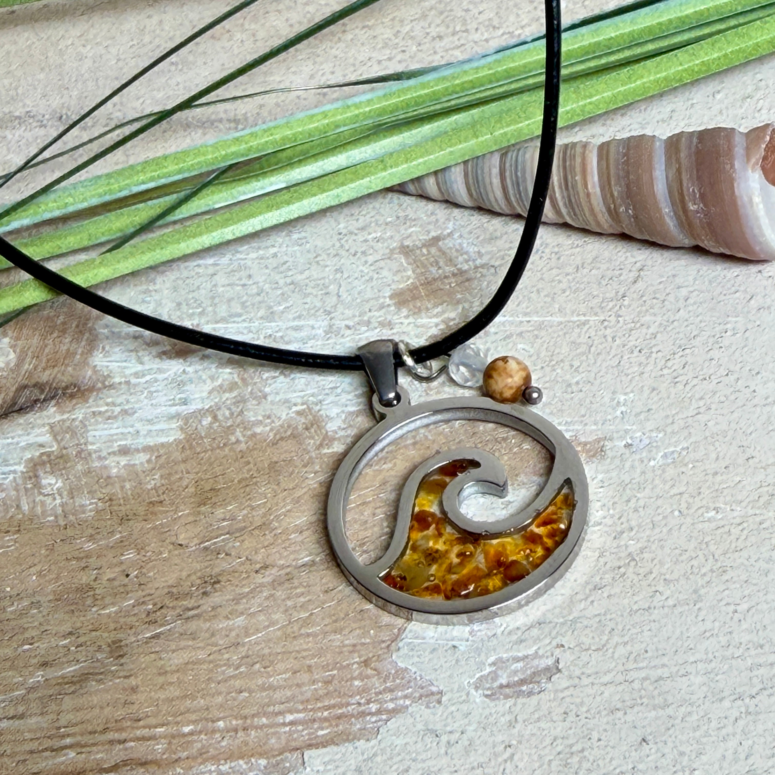 “Runder Wellenanhänger aus Edelstahl mit Bernstein-Harz-Inlay, Jaspisperle & facettiertem Bergkristall an schwarzer Lederkette (45 cm + 5 cm).”