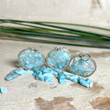 Runder Anhänger „Atlantis Dream“ aus antik-silberfarbener Zinklegierung, gefüllt mit kleinen Larimar-Edelsteinchen und klarem Resin. Die Larimarsteine zeigen sanfte Blau- und Weißtöne, die an das Meer erinnern. Durchmesser ca. 22 mm, handgefertigtes Unikat, fotografiert auf maritimem Untergrund mit kleinen Larimarsteinen und Muscheln zur Größenorientierung.