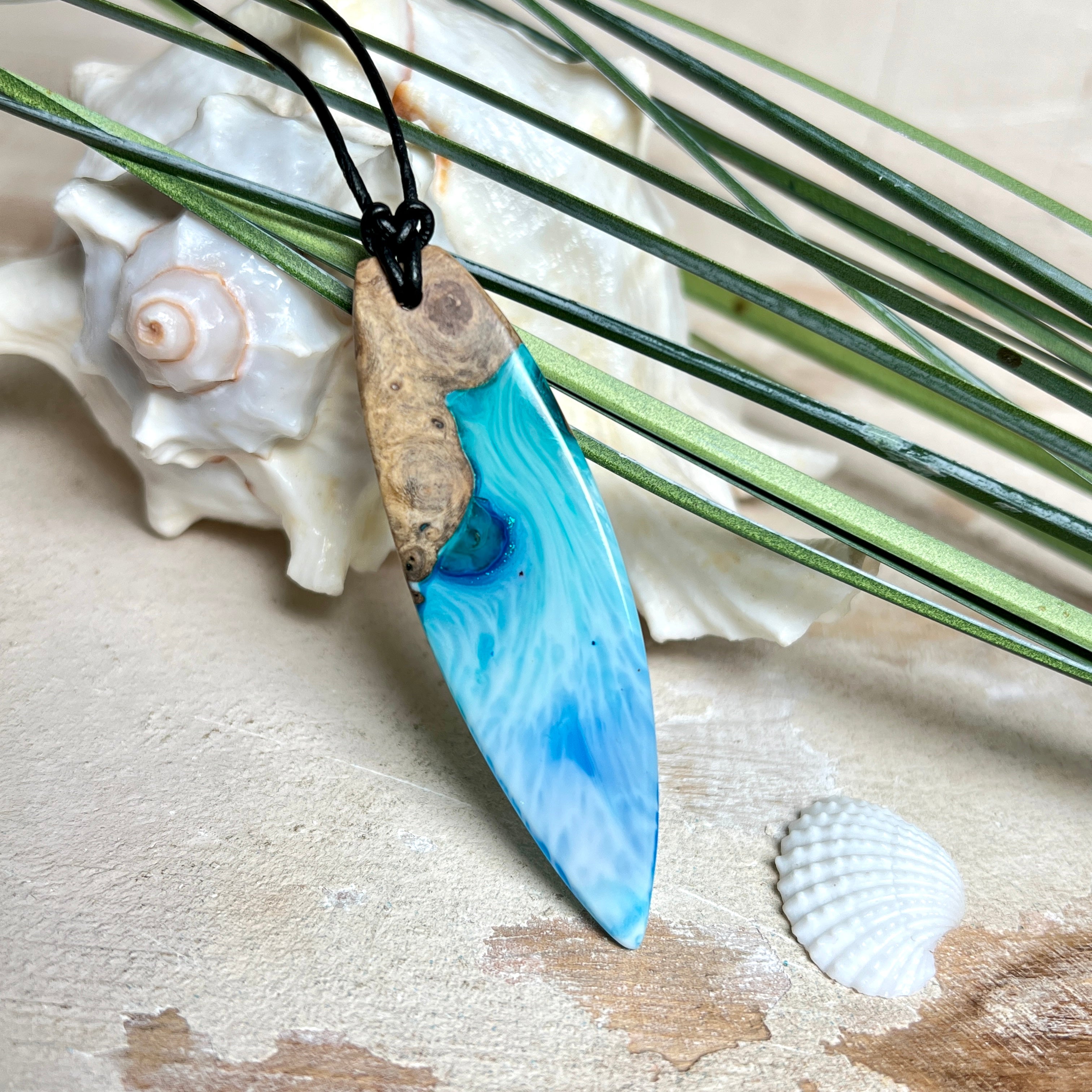 Surfbrett-Anhänger handgefertigt aus Maserholz & Harz in Blau-Weiß. Größe ca. 6,3 × 2 cm. Lederband verstellbar 26–47 cm, Schiebeknoten mit Holzperlen.