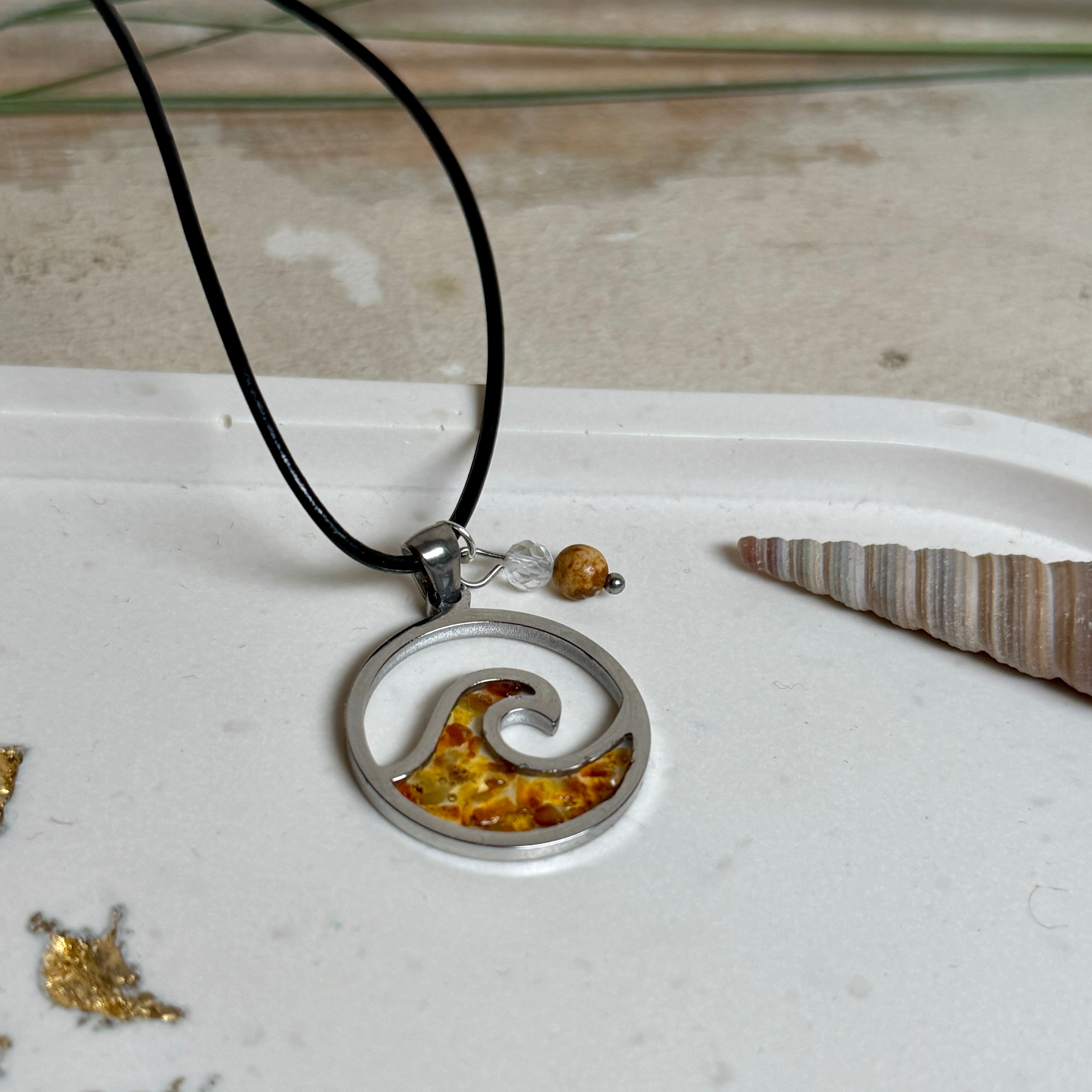 “Runder Wellenanhänger aus Edelstahl mit Bernstein-Harz-Inlay, Jaspisperle & facettiertem Bergkristall an schwarzer Lederkette (45 cm + 5 cm).”