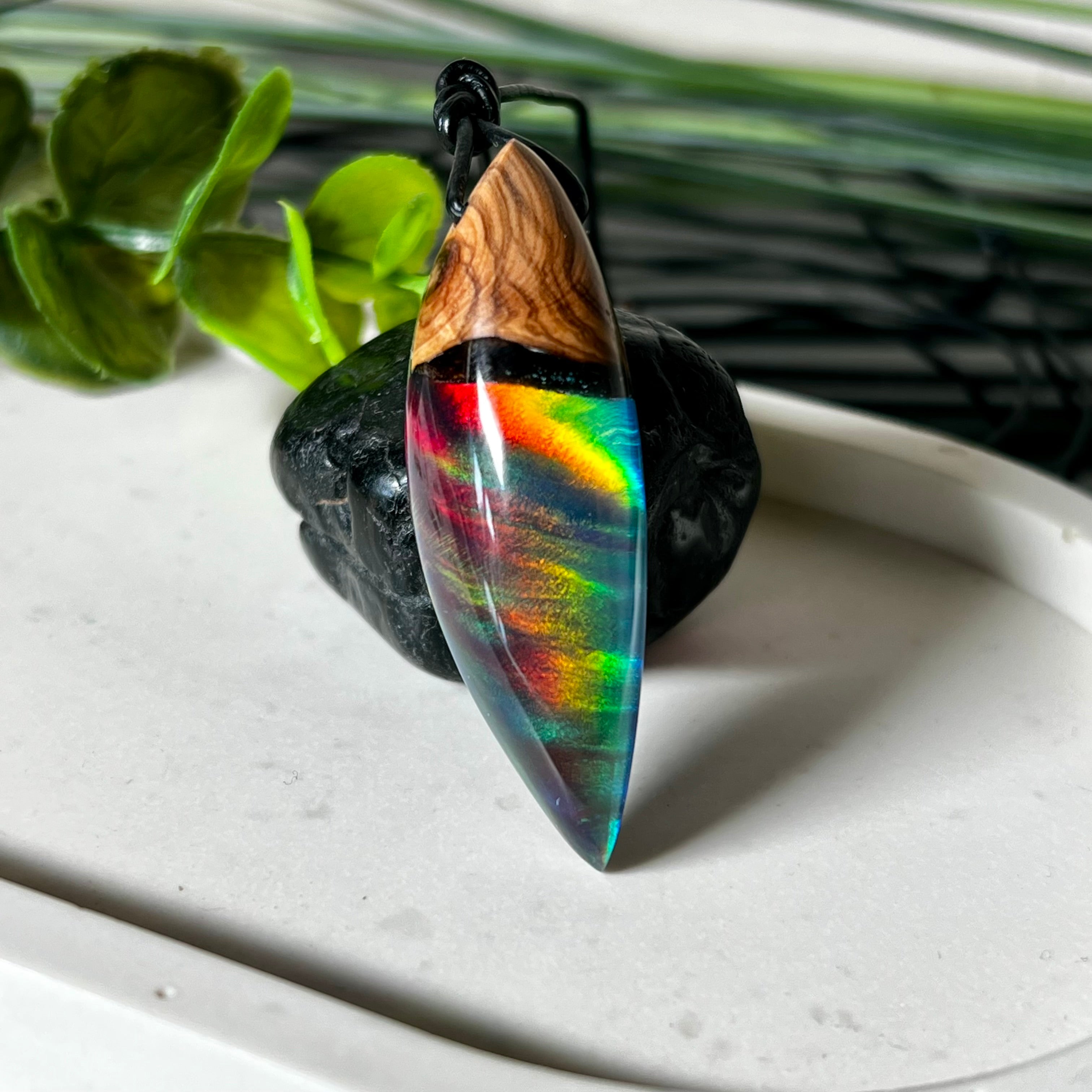 Der handgefertigte Anhänger „Celestial Flame“ kombiniert warmes Olivenholz mit glasklarem Harz und irisierendem Opal. Das einzigartige Farbspiel erinnert an Polarlichter und verleiht dem Schmuckstück eine mystische Tiefe. Die Oberfläche ist glatt poliert, der Anhänger wird an einem verstellbaren Lederband getragen – ein ausdrucksstarkes Unikat für alle, die Naturmaterialien und kreative Farben lieben.