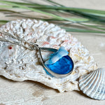 „Lagunenlicht“ – Tropfenanhänger mit handmodellierter 3D-Welle und feinem Glitzereffekt. Klarer Harzlook in Blau/Türkis, gefasst in Silber-Legierung. Größe ca. 3,5 × 2 cm. Geliefert an einer versilberten Kette (ca. 56 cm). Hochglänzend , maritimer Unikatcharakter.