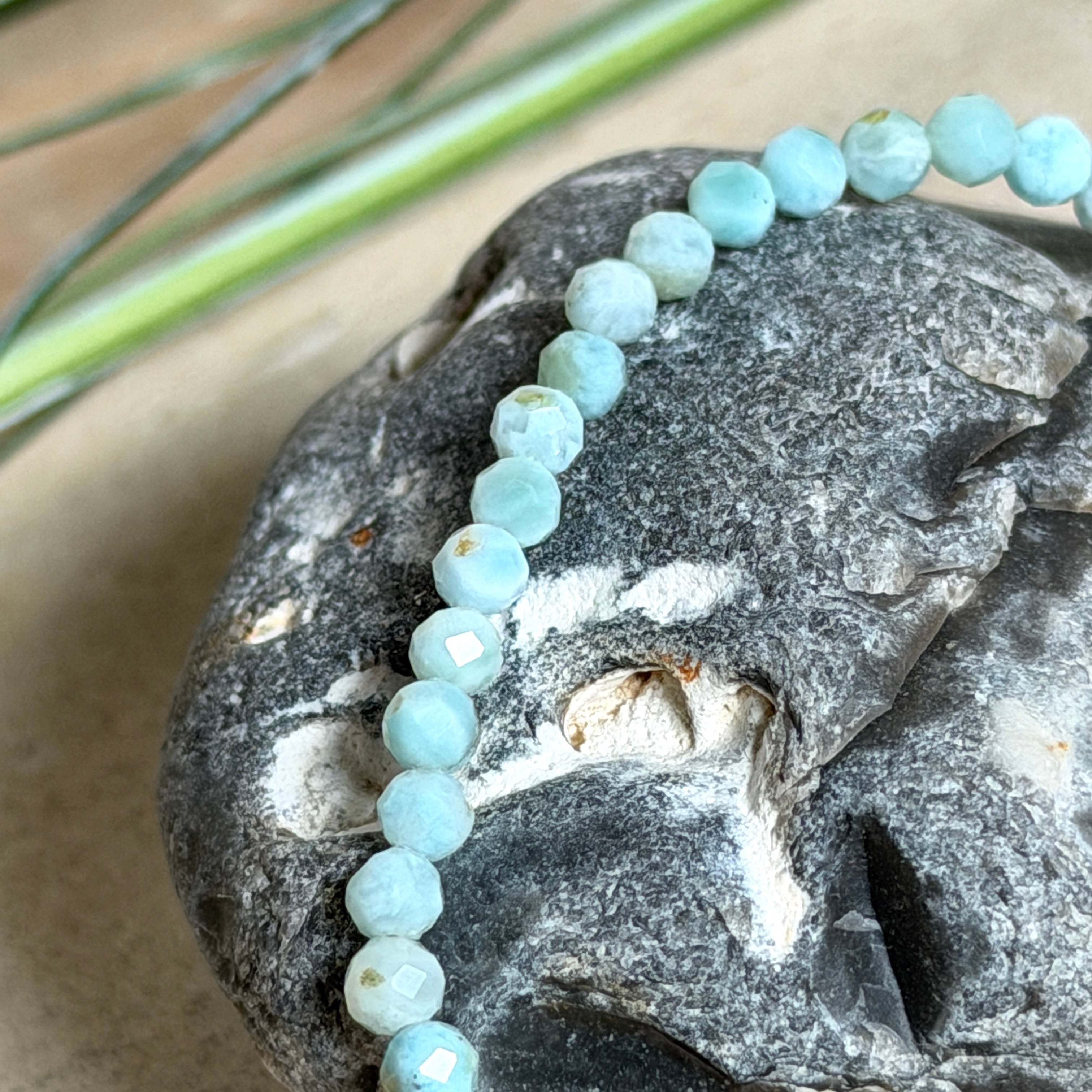 Zartes Larimar-Armband „Lagunenlicht“ mit facettierten 3 mm Perlen aus seltenem Atlantisstein auf Elastikfaden. Die kleinen Larimarsteine zeigen sanfte Blau- und Weißtöne wie Lagunenwasser. Innenumfang ca. 19 cm. Fotografiert auf Muscheln, einem dekorativen Stein und in einer schwarzen Schmuckbox von ZeitlosSchmuckDesign im maritimen Stil.
