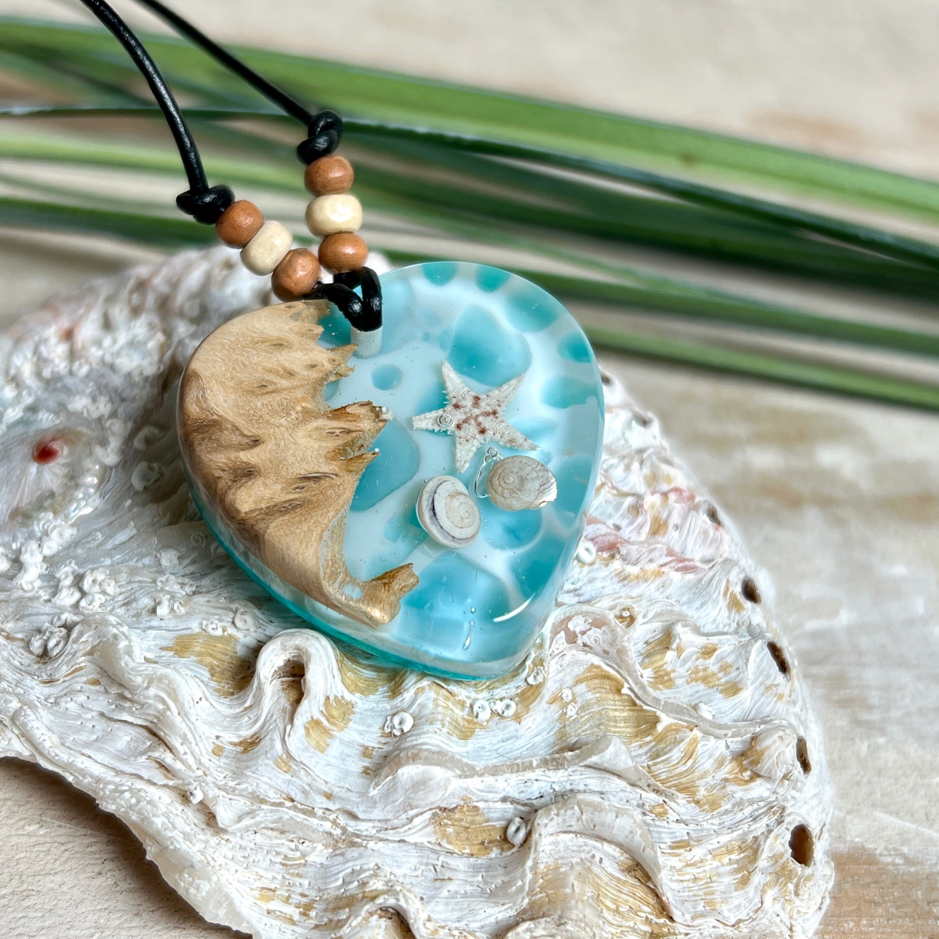 Handgefertigter Herzanhänger aus Maserholz und transparentem Ocean-Harz mit echtem Seestern und Muscheln. Die zarten Aqua-Farben erinnern an Meereswellen. Lederband verstellbar mit Holzperlen. Größe ca. 3,5 × 3,2 cm. Natürliches, maritimes Unikat von ZeitlosSchmuckDesign