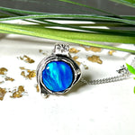 Handgemachter Anhänger mit rundem Cabochon aus Epoxidharz und schimmerndem synthetischem Opal. Die Farben changieren je nach Lichteinfall in Blau, Türkis und Grün. Der Opal sitzt in einer antik versilberten Fassung aus Messing (blei- & nickelfrei). Geliefert mit einer rhodinierten 925 Silberkette (45 cm). Jedes Stück ein Einzelstück – perfekt als stilvolles Geschenk oder persönlicher Glücksbringer.