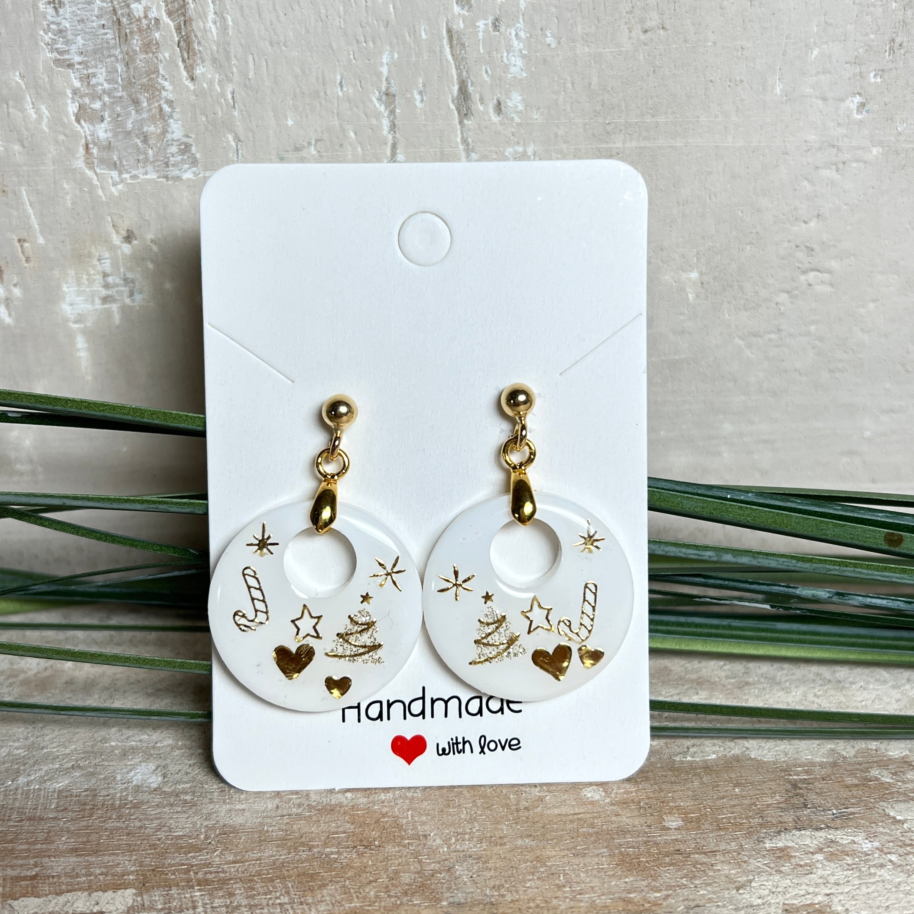Handgefertigte Ohrringe aus weißem und klarem Harz mit goldenen Weihnachtsmotiven – Sterne, Herzen, Tannenbaum und Zuckerstange. Ohrstecker aus 925 Silber vergoldet, Anhängerschlaufe vergoldet. Größe ca. 37 mm × 25 mm. Leichte, elegante Festtagsohrringe mit warmem Goldglanz und winterlicher Ausstrahlung.