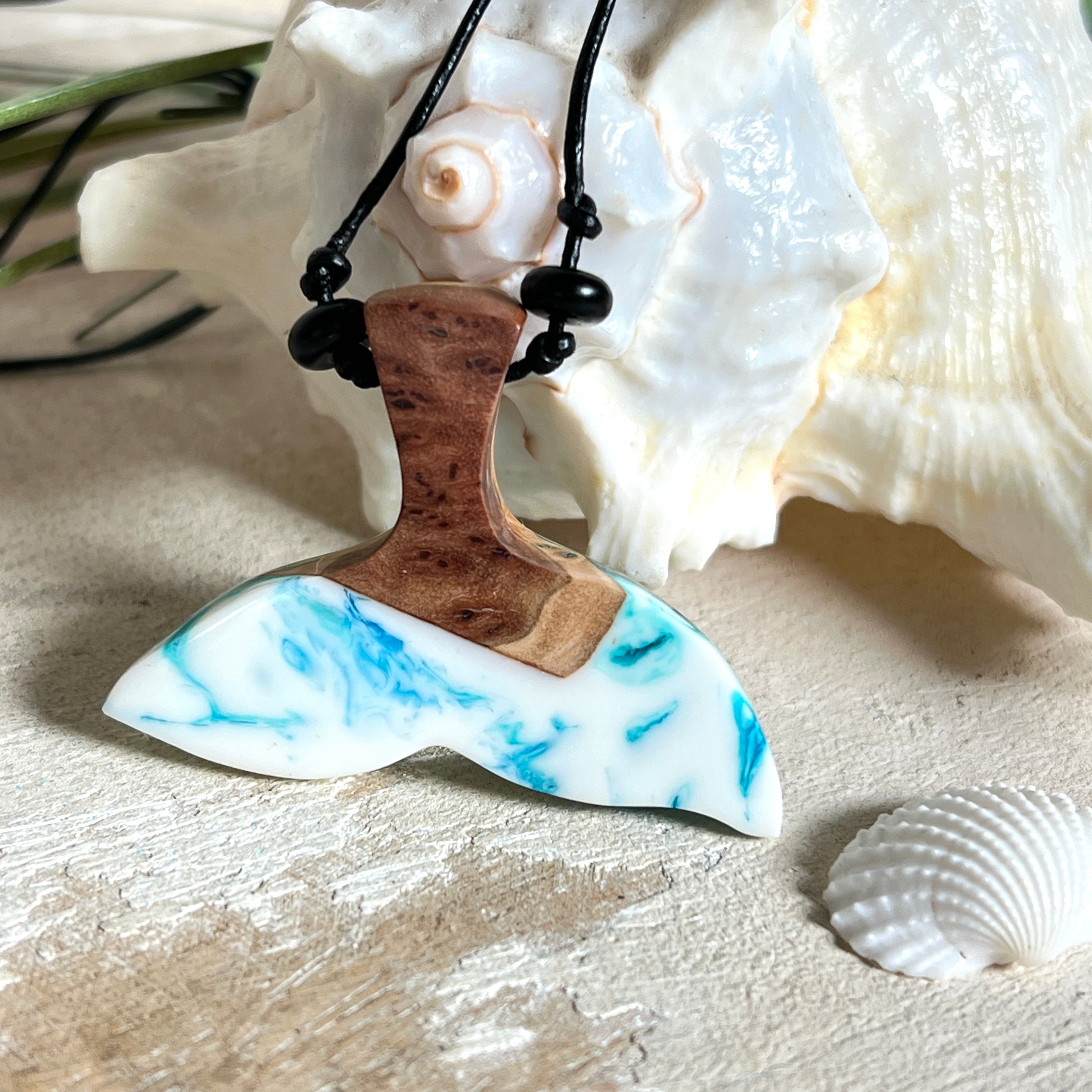 Walflossen-Anhänger „Flossenklang“ – handgefertigtes Unikat aus Maserholz und blau-weißem Harz. Die elegant geschwungene Form erinnert an die Flosse eines Wals und symbolisiert Freiheit, Stärke und Naturverbundenheit. Mit verstellbarem schwarzen Lederband und Onyxperlen gefertigt, ist jedes Stück ein individuelles Schmuckstück für Meeresliebhaber und Natursuchende. Maritimer Halsschmuck, inspiriert vom Ozean, glatt poliert und mit Liebe zum Detail von Hand gearbeitet.