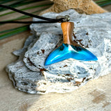 Handgefertigter Walflossen-Anhänger aus Olivenholz und Epoxidharz in Blau-Grün-Weiß, polierte Oberfläche, Edelstahl-Öse. Schwarze Lederkette 45 cm mit Edelstahl-Karabinerverschluss und 5 cm Edelstahl-Verlängerung. Anhängergröße ca. 2,5 × 3,2 cm, maritime Produktfotografie.