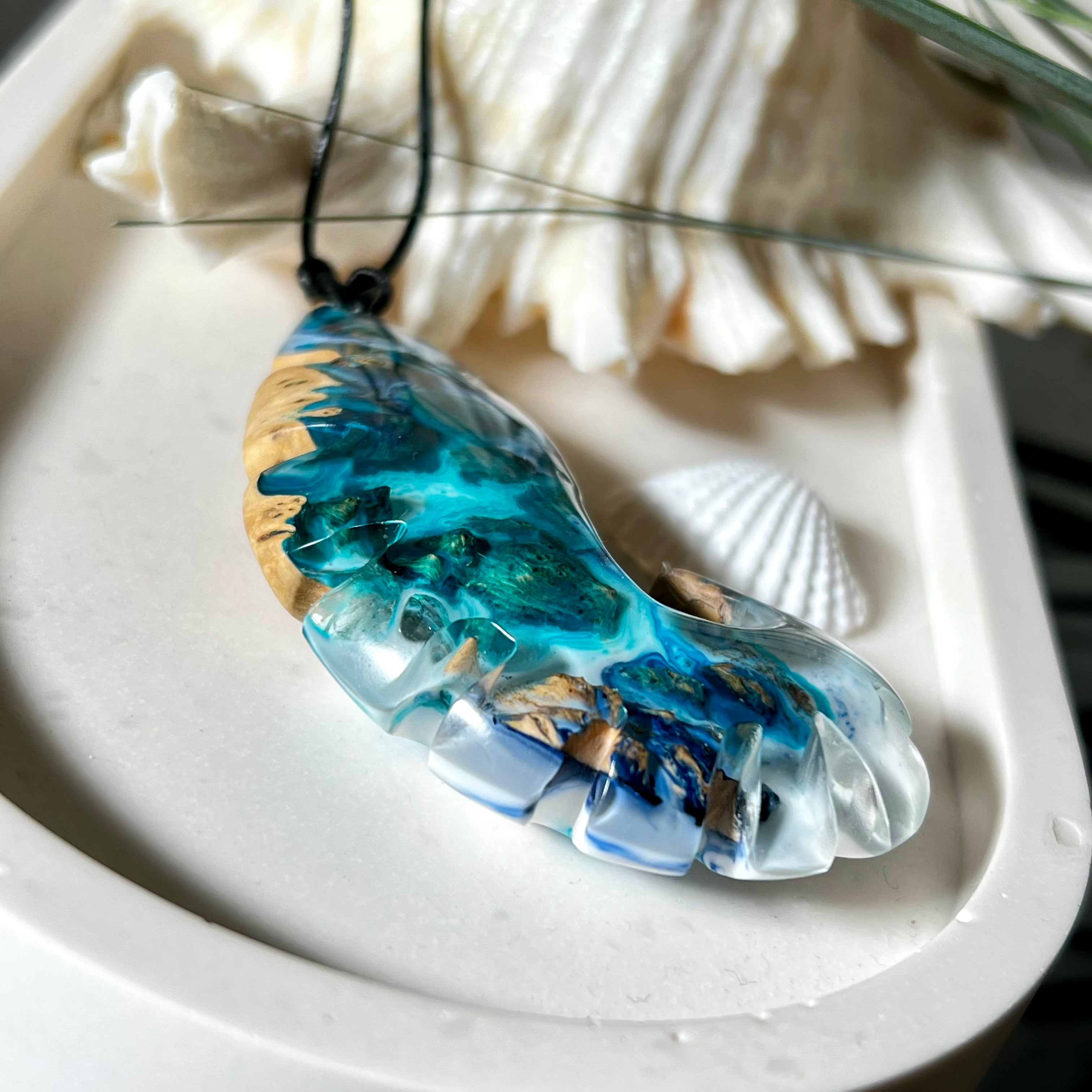 Ocean Nautilus Halskette – handgefertigter Anhänger aus  Epoxidharz und edlem Maserholz in kräftigem Blau, Türkis und Weiß, geformt wie eine stilisierte Nautilus-Muschel. Die einzigartige Maserung des Holzes trifft auf transparente Tiefenwirkung des Harzes. Der ca. 7 cm große Anhänger hängt an einem verstellbaren Lederband mit dekorativen Holzperlen (26–48 cm). Jedes Stück ist ein maritimes Unikat, inspiriert von der Magie des Meeres.