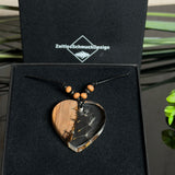 Handgefertigter Herzanhänger aus warm gemasertem Olivenholz und kristallklarem Epoxidharz mit schwebenden Pusteblumensamen. Schwarzes, verstellbares Lederband mit Schiebeknoten und naturfarbenen Holzperlen, Anhänger ca. 3,5 × 3,3 cm. Naturnaher Unikatschmuck von ZeitlosSchmuckDesign.