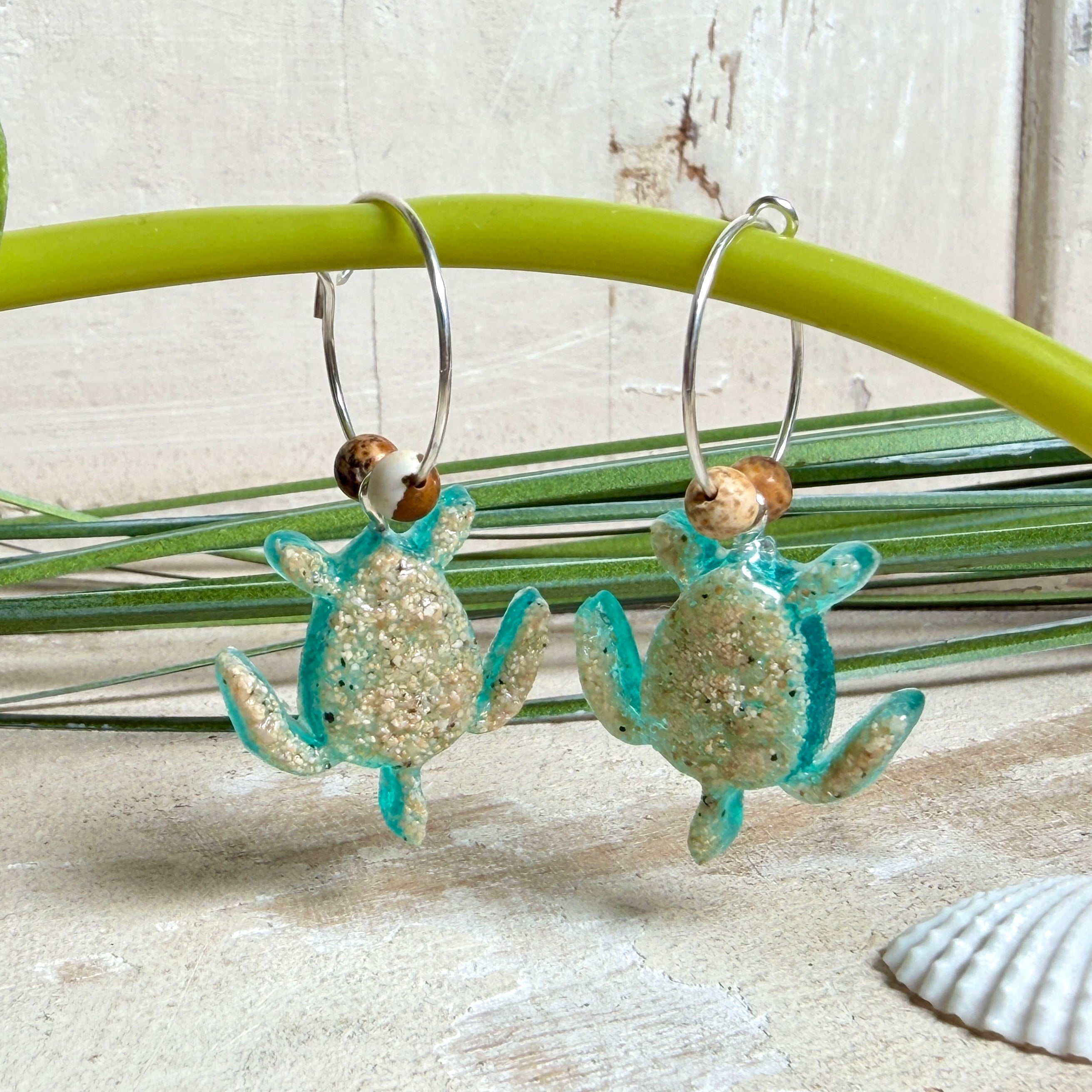 Türkisfarbene Schildkröten-Creolen an feinen 16-mm-Ringen aus 925 Silber, jeweils mit echtem Strandsand im Harz eingebettet und mit kleinen Jaspis-Edelsteinperlen verziert; handgefertigtes Unikat mit sommerlich-maritimem Look, fotografiert als Freisteller, Nahaufnahme oder auf dekorativem Untergrund.