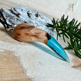 Handgefertigter Anhänger aus Edelholz und transparent-türkisblauem Epoxidharz, glatt poliert. Größe ca. 6,7 × 2,0 cm. Mit Edelstahlöse an schwarzer Lederkette (45 cm + 5 cm Edelstahl-Verlängerung, Karabiner). Maritimer, moderner Unisex-Schmuck mit natürlicher Holzmaserung; kleine Lufteinschlüsse sind charakteristisch.