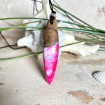 Handgefertigter Surfbrett-Anhänger aus Nussbaumholz und fluoreszierendem Epoxidharz in Pink, Blau und Weiß. Der Anhänger leuchtet zart bei Schwarzlicht und wird an einem verstellbaren Lederband (25–44 cm) mit Holzperlen getragen. Ein maritimes Unikat – ideal für Surfer und Naturliebhaber.