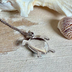 Feine Kette aus rhodiniertem 925 Silber mit Wasserschildkröten-Anhänger. Der ca. 25 x 18 mm große Anhänger zeigt eine Schildkröte, deren Panzer aus mehreren hellblauen Larimar-Inlays besteht. Seltener, kostbarer Larimar mit typischen wolkigen Strukturen, an einer ca. 45 cm langen, 1 mm starken, auf Platin rhodinierten Silberkette. Fotografiert in schwarzer Schmuckbox und vor maritimer Dekoration mit Muscheln.