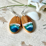 Handgefertigte Ohrringe „Wave Harmony“ aus Olivenholz und Epoxidharz in Blau-, Türkis- und Weißtönen. Das Design erinnert an Meereswellen am Strand. Jeder Ohrring ist ein Unikat mit individueller Maserung. Versilberte, nickelfreie und bleifreie Anhängerschlaufe, 925 Silber Ohrhaken. Maritimer Schmuck – perfekt für Meerliebhaber und als edles Geschenk.