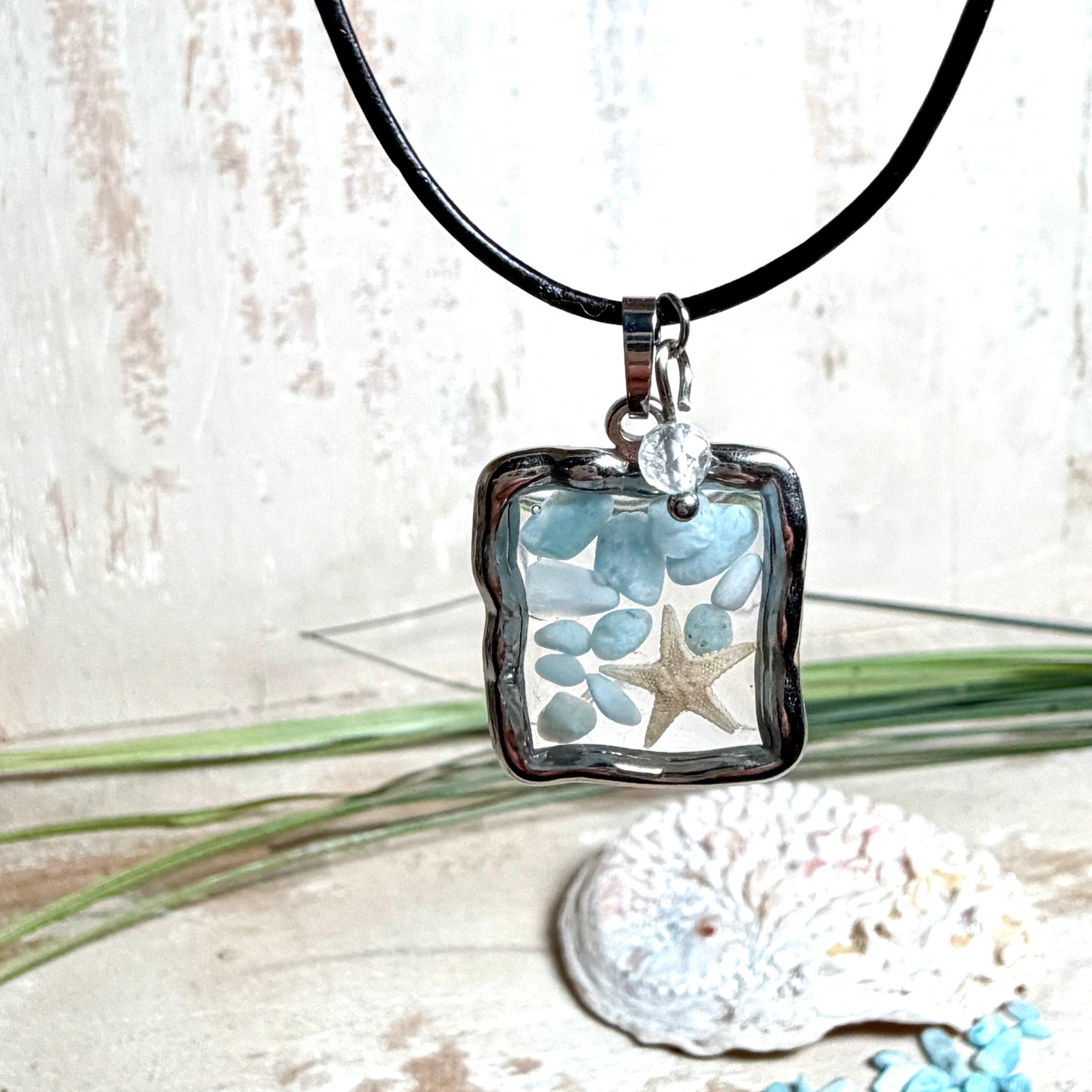 Quadratischer Larimar-Mosaik Anhänger im Edelstahlrahmen mit Seestern-Element und facettierter Bergkristall-Perle, eingebettet in Harz, an schwarzer Lederkette.