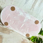 Schmucktablett aus Jesmonite in zartem Rosa-Weiß-Marmor. Handgegossenes, ovales Deko-Tablett mit glatter Oberfläche und Korkfüßen. Perfekt als Ablage für Schmuck, Schlüssel, Brille oder Dekoobjekte. Jedes Stück ein liebevoll gefertigtes Unikat in der Größe 17,5 × 9,5 × 1,7 cm.
