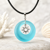 TURQUOISE BAY Seeglas Halskette mit türkisem Donut-Anhänger und Sonnen-Charm aus Edelstahl, handgefertigter maritimer Boho Schmuck für Frauen, sommerliche Kette mit schwarzer Lederschnur.