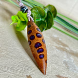 Handgefertigter Anhänger aus einem australischen Banksiazapfen mit eingelassenem metallic-violettem Harz. Der ovale, tropfenförmige Anhänger ist ca. 5,5 cm lang und wird mit einem verstellbaren Baumwollband geliefert. Jedes Stück zeigt die einzigartige natürliche Struktur des Zapfens und schimmert in satten Lilatönen – ein stilvoller Schmuck mit organischem Charakter.