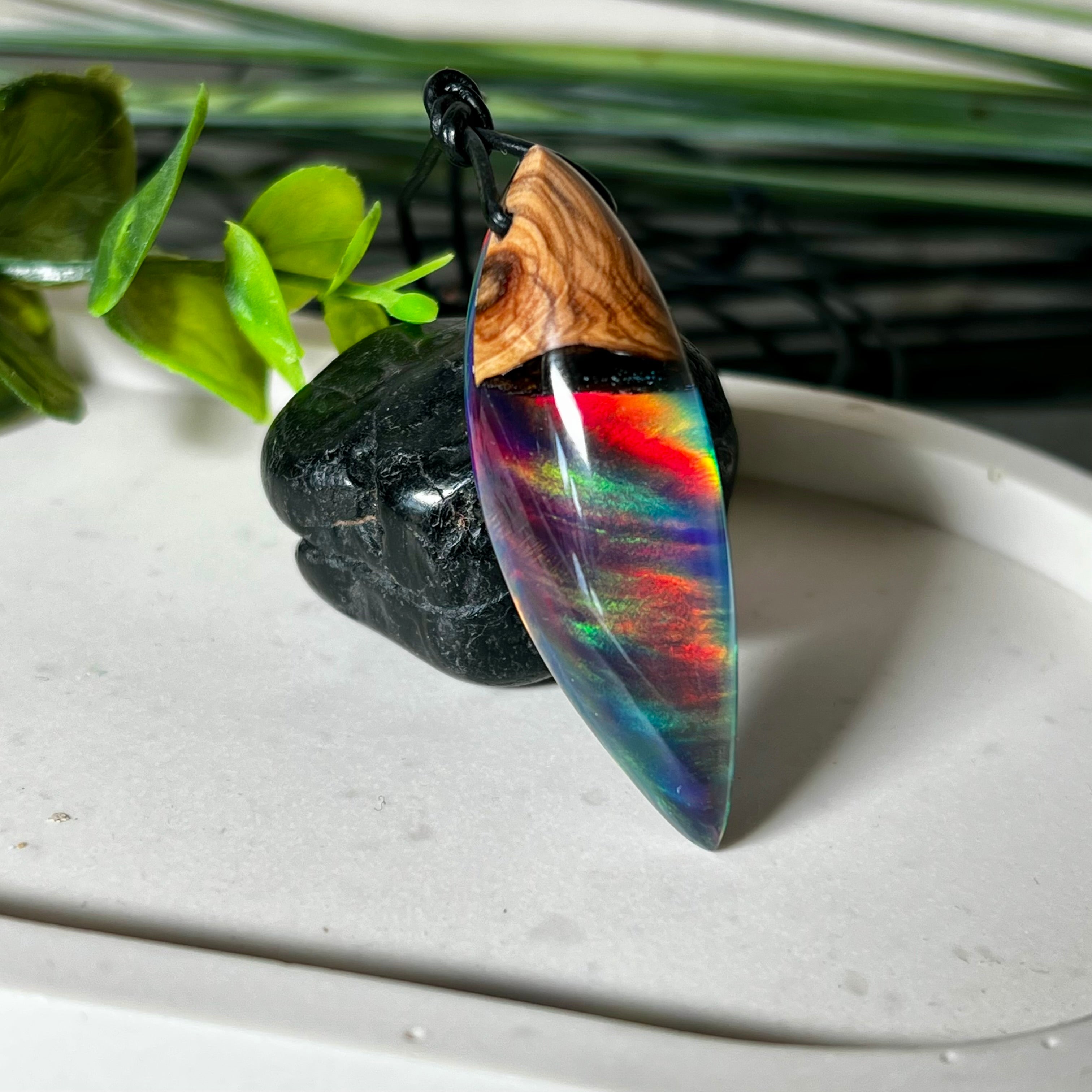 Der handgefertigte Anhänger „Celestial Flame“ kombiniert warmes Olivenholz mit glasklarem Harz und irisierendem Opal. Das einzigartige Farbspiel erinnert an Polarlichter und verleiht dem Schmuckstück eine mystische Tiefe. Die Oberfläche ist glatt poliert, der Anhänger wird an einem verstellbaren Lederband getragen – ein ausdrucksstarkes Unikat für alle, die Naturmaterialien und kreative Farben lieben.