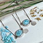 Verstellbares Edelstahlarmband mit Zirkoniasteinchen und Schiebeverschluss und rundem Anhänger (ca. 2,5 × 1,7 cm) mit echten Larimar-Edelstein-Splittern in Harz. Zusätzlich ein Charm „Blume des Lebens“ aus 925 Silber. Handgefertigtes Unikat in Türkis- und Meeresblautönen – Schmuckstück in Nahaufnahme bzw. als Tragebild am Handgelenk.