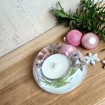 Runder Teelichthalter aus klarem Epoxidharz, Durchmesser ca. 7 cm, Höhe ca. 4 cm. Im Harz sind rosa Weihnachtskugeln, ein Stern, eine Schneeflocke, ein Tannenbaum, künstliche Tannennadeln und feiner Glitzer eingegossen. Vertiefung für ein Teelicht in der Mitte, Unterseite mit vier Korkpads als Möbelschoner. Fotografiert auf Holz mit Tannenzweig und rosa Kugeln als weihnachtliche Dekoration