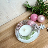 Runder Teelichthalter aus klarem Epoxidharz, Durchmesser ca. 7 cm, Höhe ca. 4 cm. Im Harz sind rosa Weihnachtskugeln, ein Stern, eine Schneeflocke, ein Tannenbaum, künstliche Tannennadeln und feiner Glitzer eingegossen. Vertiefung für ein Teelicht in der Mitte, Unterseite mit vier Korkpads als Möbelschoner. Fotografiert auf Holz mit Tannenzweig und rosa Kugeln als weihnachtliche Dekoration