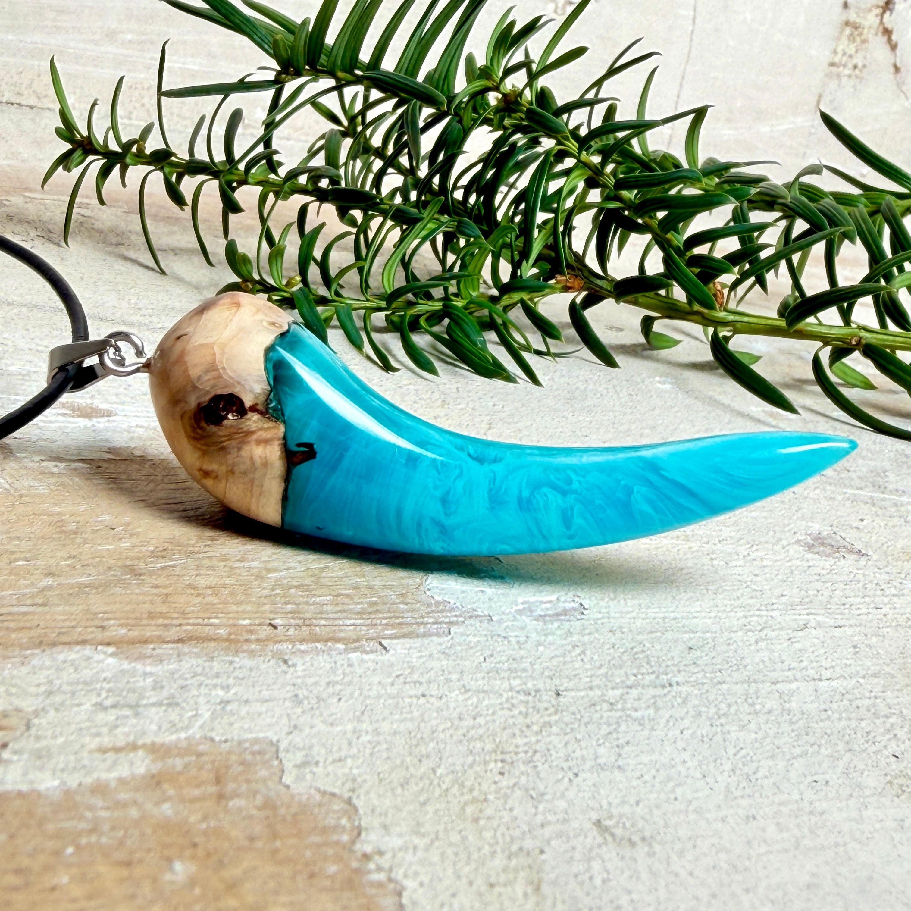 Handgefertigter Anhänger aus Edelholz und transparent-türkisblauem und weißen Epoxidharz, glatt poliert. Größe ca. 6,5 × 2,0 cm. Mit Edelstahlöse an schwarzer Lederkette (45 cm + 5 cm Edelstahl-Verlängerung, Karabiner). Moderner, unisex tragbarer Schmuck mit natürlicher Holzmaserung; kleine Lufteinschlüsse sind charakteristisch.