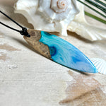 Surfbrett-Anhänger handgefertigt aus Maserholz & Harz in Blau-Weiß. Größe ca. 6,3 × 2 cm. Lederband verstellbar 26–47 cm, Schiebeknoten mit Holzperlen.