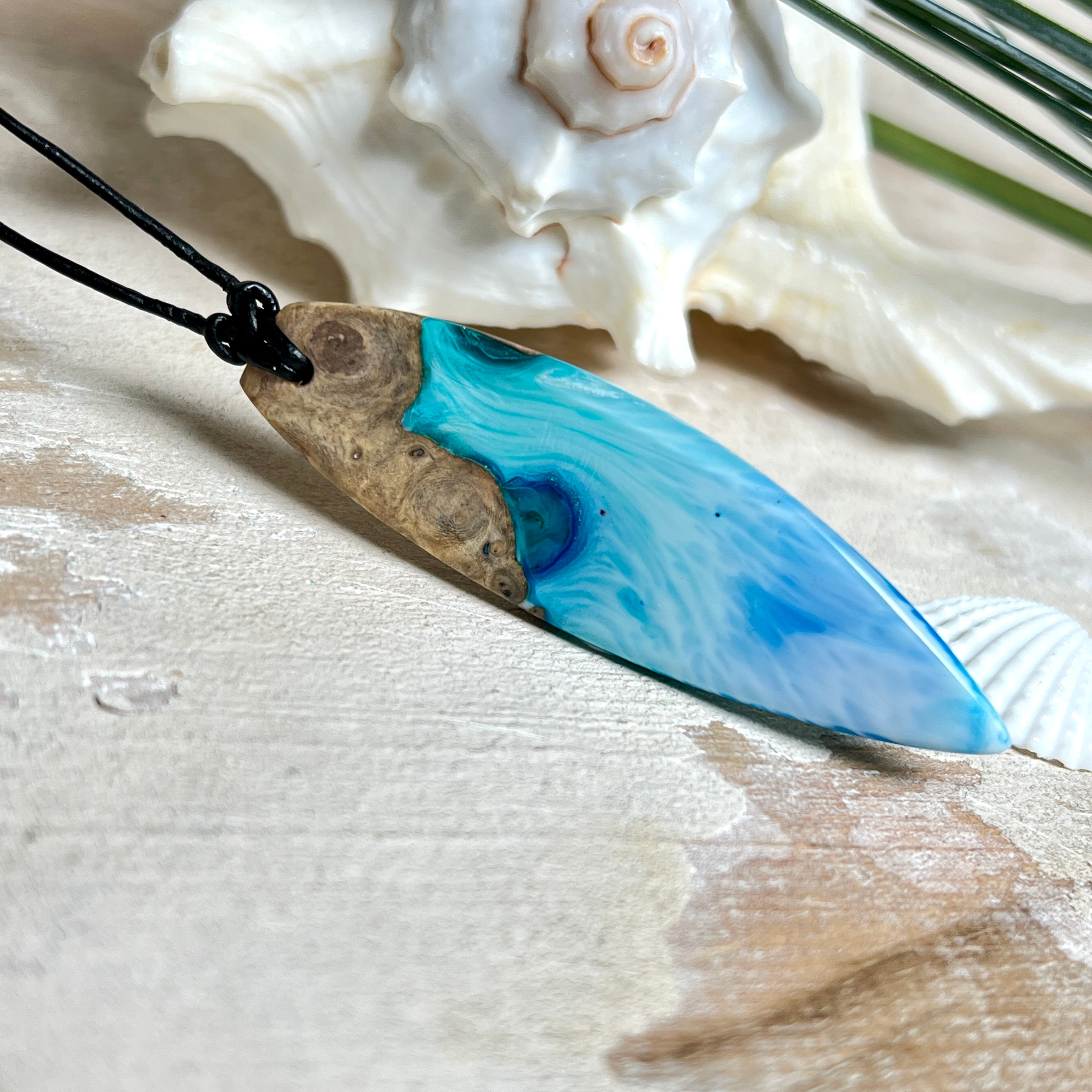 Surfbrett-Anhänger handgefertigt aus Maserholz & Harz in Blau-Weiß. Größe ca. 6,3 × 2 cm. Lederband verstellbar 26–47 cm, Schiebeknoten mit Holzperlen.
