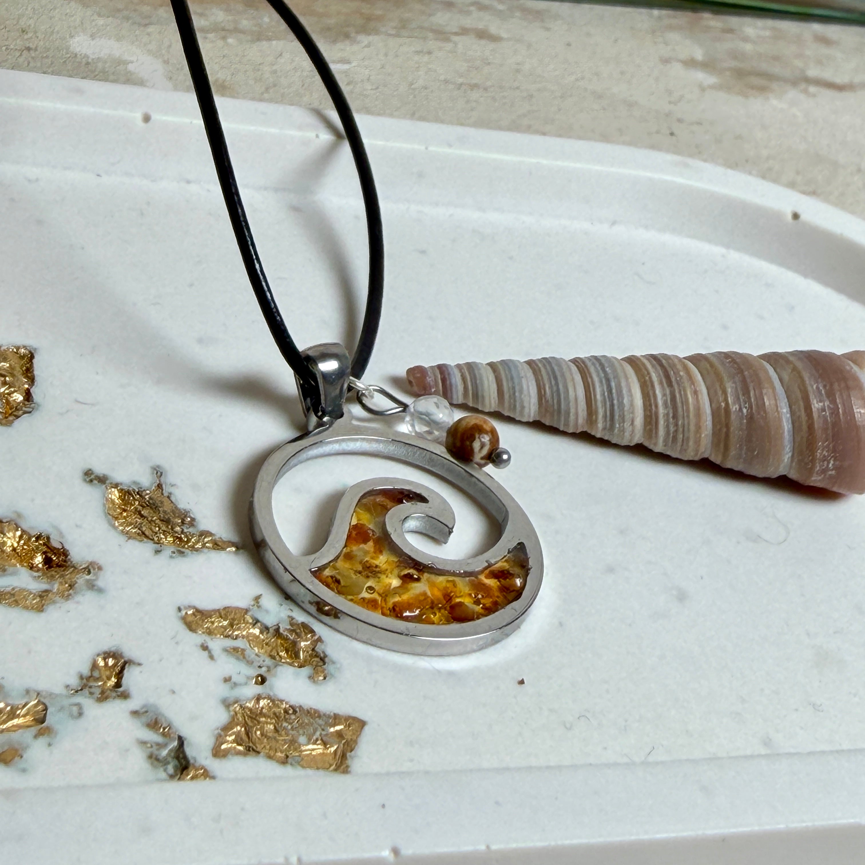 “Runder Wellenanhänger aus Edelstahl mit Bernstein-Harz-Inlay, Jaspisperle & facettiertem Bergkristall an schwarzer Lederkette (45 cm + 5 cm).”