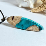 Handgefertigte Surfbrett Kette aus Maserholz und türkisfarbenem Resin mit Edelstahl Anhängerschlaufe an schwarzer Lederkette mit Karabiner und Verlängerung. Filigraner Ocean Anhänger inspiriert von Meer und Wellen, natürlicher Unikat Schmuck für Damen und Herren.