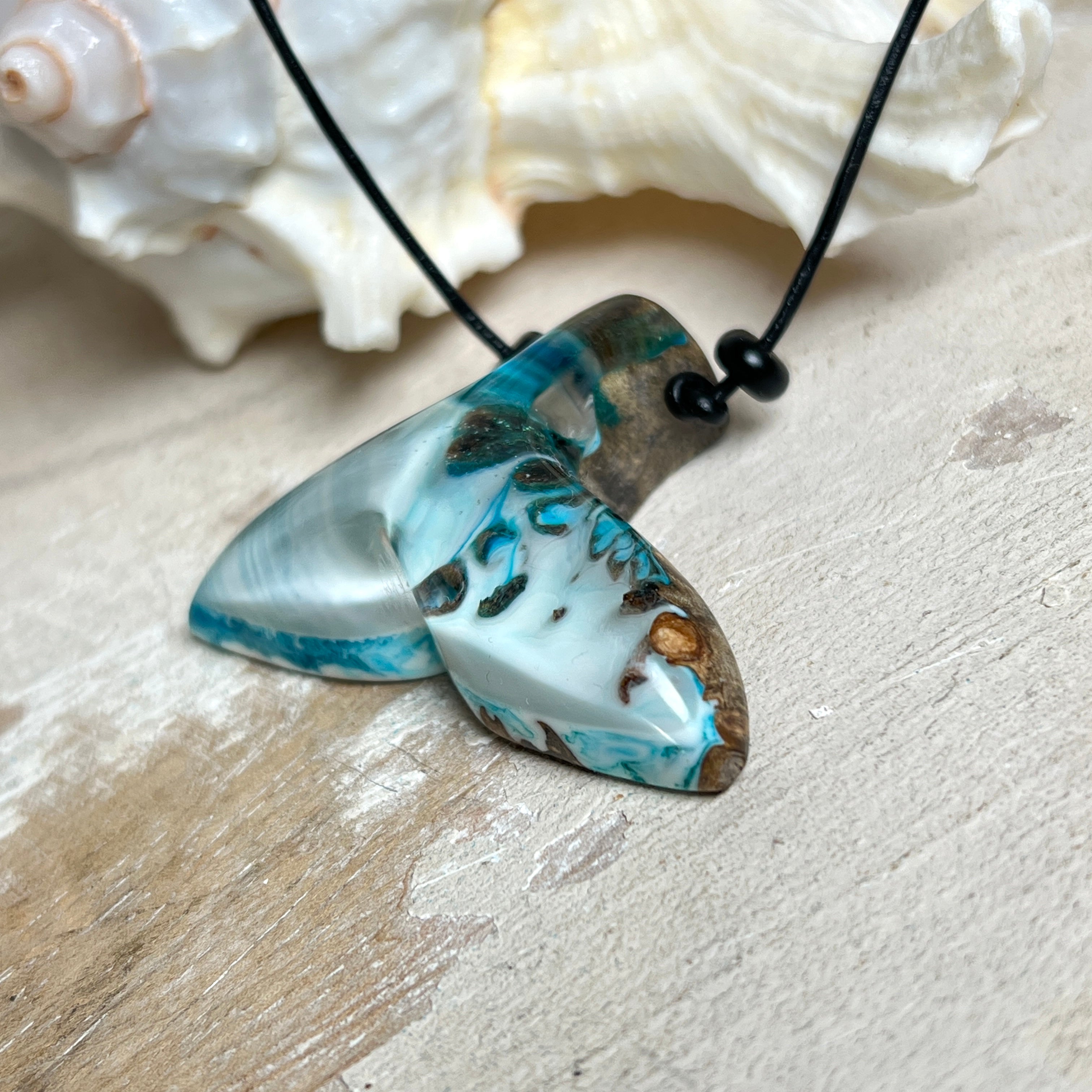 Handgefertigter Walflossen-Anhänger „Flossenklang“ aus Maserholz und türkis-blau-grau-weiß marmoriertem Epoxidharz an verstellbarem Lederband. Maritime Kette als Unikatschmuck für Meeresliebhaber und Wal-Fans, hochwertig poliert, präsentiert vor Muscheldeko und in Schmuckbox von ZeitlosSchmuckDesign.