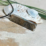 Rechteckiger Stabanhänger aus Maserholz und glasklarem Epoxidharz in tiefen Blau- und Türkistönen mit organischer Lagunen/Riff-Optik. Hochglanzpoliert, ca. 4,6 × 1,2 cm. Der Anhänger hängt an einer schwarzen Lederkette mit Edelstahl-Karabiner und 5-cm-Verlängerung (45 + 5 cm); die Anhängerschlaufe ist ebenfalls aus Edelstahl. Handgefertigtes Unikat, Lieferung in edler Schmuckbox – maritimer Look.