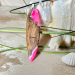 Handgefertigter Surfbrett-Anhänger „Pink Glow“ aus edlem Olivenholz und fluoreszierendem Epoxidharz in Pink & Weiß. Fluoreszierend bei Schwarzlicht, mit Edelstahl-Anhängerschlaufe und schwarzer Lederkette (45 cm + 5 cm Verlängerung). Ein maritimes Unikat – perfekt als Geschenk für Surfer und Meeresliebhaber.