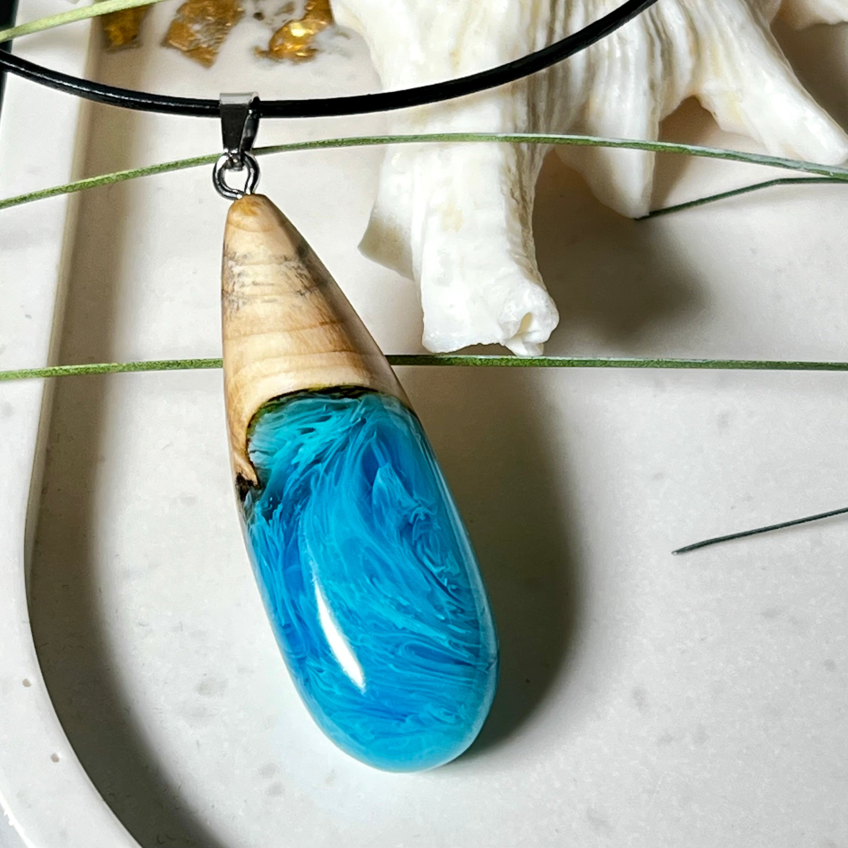Tropfenförmiger Anhänger aus Maserholz und Harz in leuchtenden Blautönen und Weiß. Inspiriert vom Meer, in Handarbeit gegossen,gesägt, geschliffen und hochglanzpoliert. Mit verstellbarer Lederkette (45 + 5 cm) und Edelstahlkarabiner. Jeder Anhänger ist ein Unikat mit natürlicher Maserung. Ein maritimes Schmuckstück für Naturfreunde und alle, die das Wasser lieben.