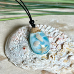 Handgefertigter Tropfenanhänger aus Maserholz und klarem Epoxidharz in Aquatönen. Im Harz sind echte Muscheln und ein kleiner Seestern eingebettet. Durch die besondere Mehrschicht-Gießtechnik wirkt es, als würden die Muscheln im Wasser schweben. Größe ca. 3,8 × 2 cm. Verstellbares Lederband (24–44 cm) mit Holzperlen. Maritimes Unikat.