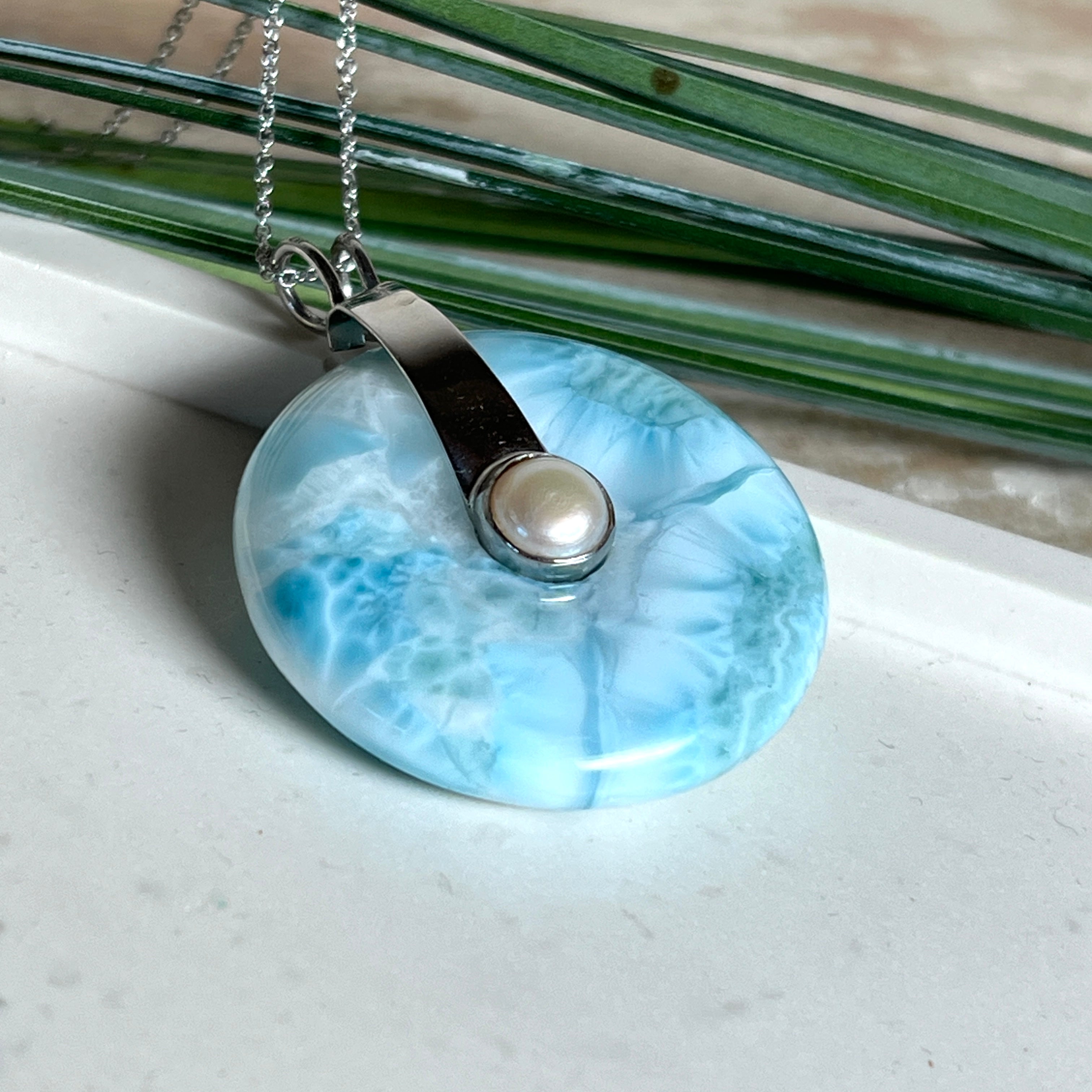 
Echter Larimar-Donut (42 mm) mit Süßwasserperle, gefasst in rhodiniertem 925 Sterlingsilber. Mit 45 cm langer, rhodinierter Silberkette. Selten, edel & handgefertigt – inspiriert vom Blau der Karibik.