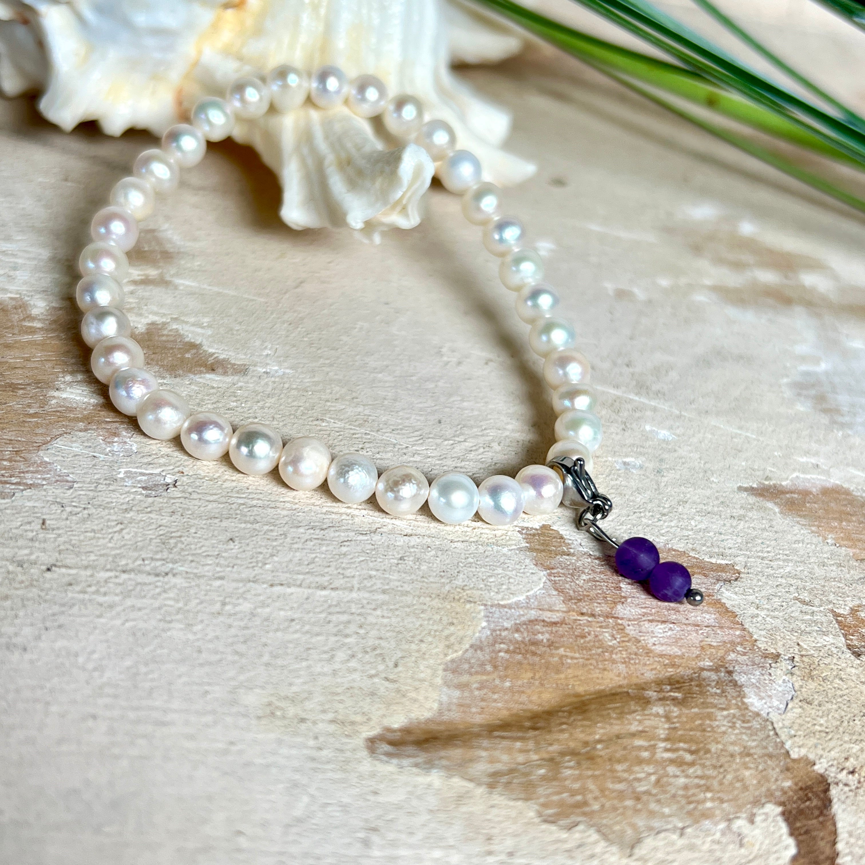 Handgefertigtes Armband „Sea Harmony“ mit schimmernden Süßwasserperlen (Ø ca. 6–7 mm), jede Perle ein Unikat. Auf elastischem Band gefädelt, mit einem filigranen Charmanhänger aus  Amethyst-Perlen, befestigt an einem robusten Edelstahl-Karabiner. Ein Schmuckstück voller Eleganz, maritimer Harmonie und symbolischer Tiefe – ideal als Geschenk oder als stilvolles Accessoire.