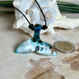 Handgefertigter Walflossen-Anhänger „Flossenklang“ aus Maserholz und türkis-blau-grau-weiß marmoriertem Epoxidharz an verstellbarem Lederband. Maritime Kette als Unikatschmuck für Meeresliebhaber und Wal-Fans, hochwertig poliert, präsentiert vor Muscheldeko und in Schmuckbox von ZeitlosSchmuckDesign.