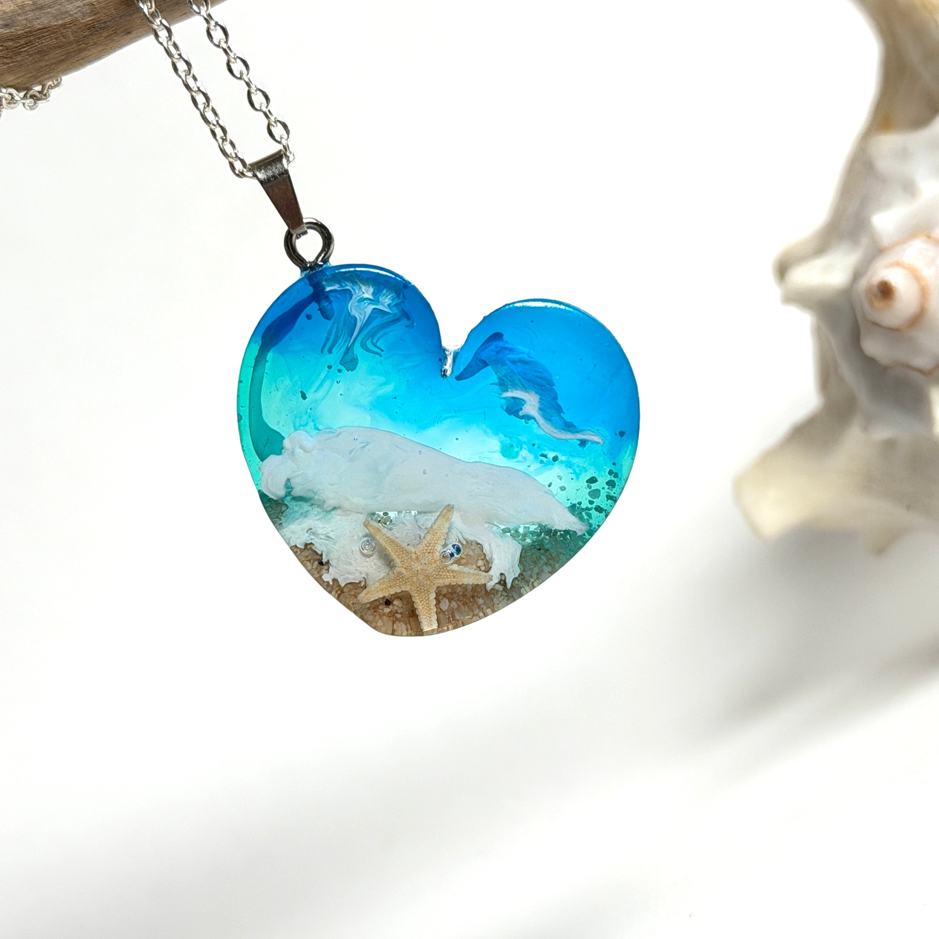 Ein herzförmiger Anhänger mit einer ganzen Ozeanwelt darin: Welle, Sand und Seestern in leuchtendem Blau und Türkis – handgegossen, einzigartig, unvergesslich. Mit versilberter Kette (46 cm) und Edelstahl-Karabiner.