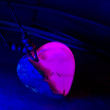 Handgefertigter Herzanhänger aus Olivenholz und leuchtend pinkem Epoxidharz mit eingeschlossenen Pusteblumensamen. Verstellbares braunes Lederband mit Holzperlen, Anhänger ca. 3,5 × 3,3 cm groß. Das Harz leuchtet dezent unter Schwarzlicht. Ein einzigartiges Unikat von ZeitlosSchmuckDesign, inspiriert von Kindheitsglück und Pusteblumen.