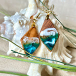 Handgefertigte Ohrringe „Ocean Diamond“ aus Olivenholz und Epoxidharz in Diamantform. Türkis-, Blau- und Weißtöne bilden ein wellenartiges Design, inspiriert vom Meer. Jeder Ohrring ist ein Unikat mit individueller Maserung. Vergoldete, nickelfreie und bleifreie Anhängerschlaufe, 925 Sterling Silber Ohrhaken. Maritimer Schmuck für Meerliebhaber und besondere Anlässe.