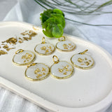 Gold-colored pendant with gold flakes, background in white and fluorescent under black light, birthday, gift