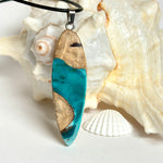 Handgefertigte Surfbrett Kette aus Maserholz und türkisfarbenem Resin mit Edelstahl Anhängerschlaufe an schwarzer Lederkette mit Karabiner und Verlängerung. Filigraner Ocean Anhänger inspiriert von Meer und Wellen, natürlicher Unikat Schmuck für Damen und Herren.